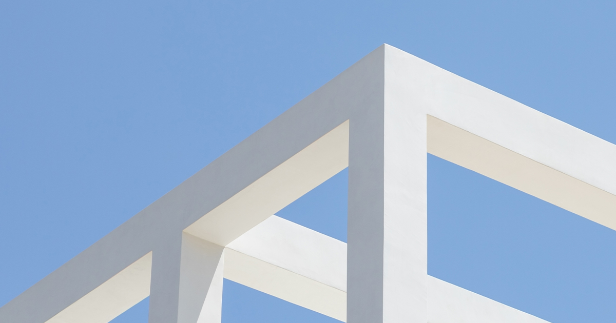 White geometric structure with sharp angles stands against a clear blue sky, creating a minimalist architectural scene with clean lines and bright contrast.